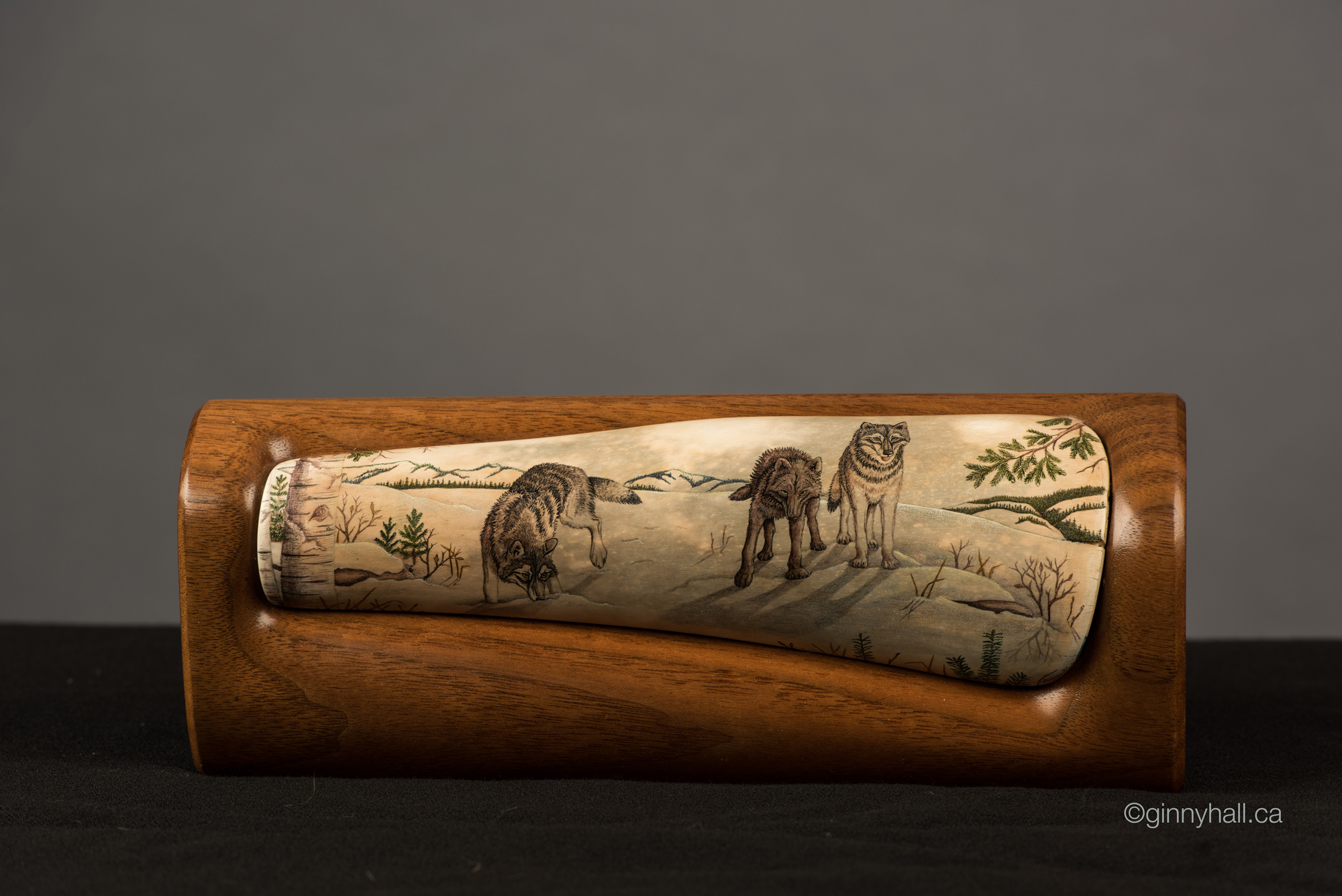 A scrimshaw peice by Ginny Hall depicting three wolves in a snowy forest.